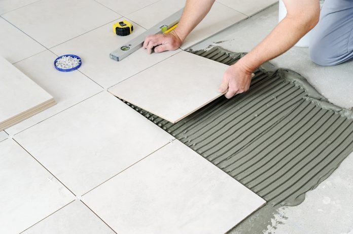 The hands of the worker are laying the ceramic tile on the floor.