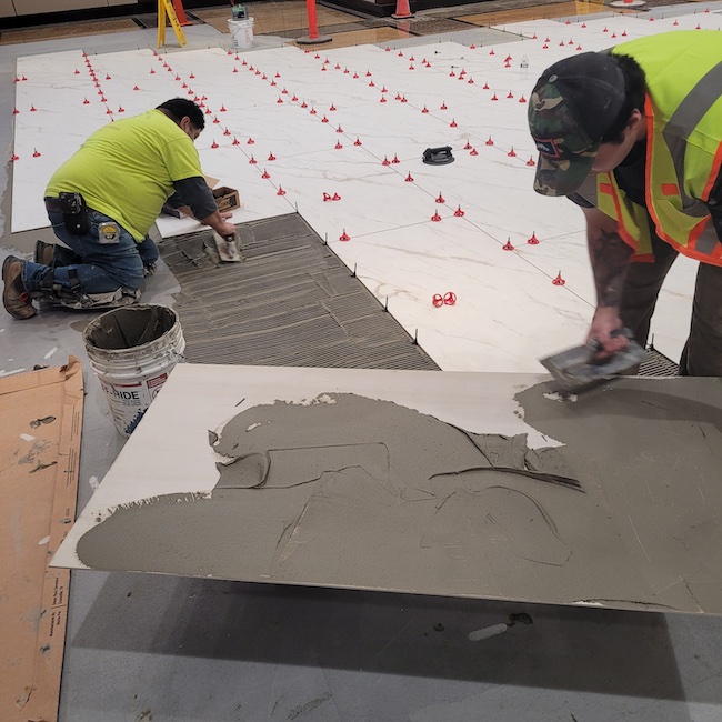 Flat-back troweling – or burn in – is applying a thin layer of mortar on the back of the tile. It can help compensate a little for edge warpage in large-format tile and will help create better bonding to the properly-troweled tile mortar on the substrate.